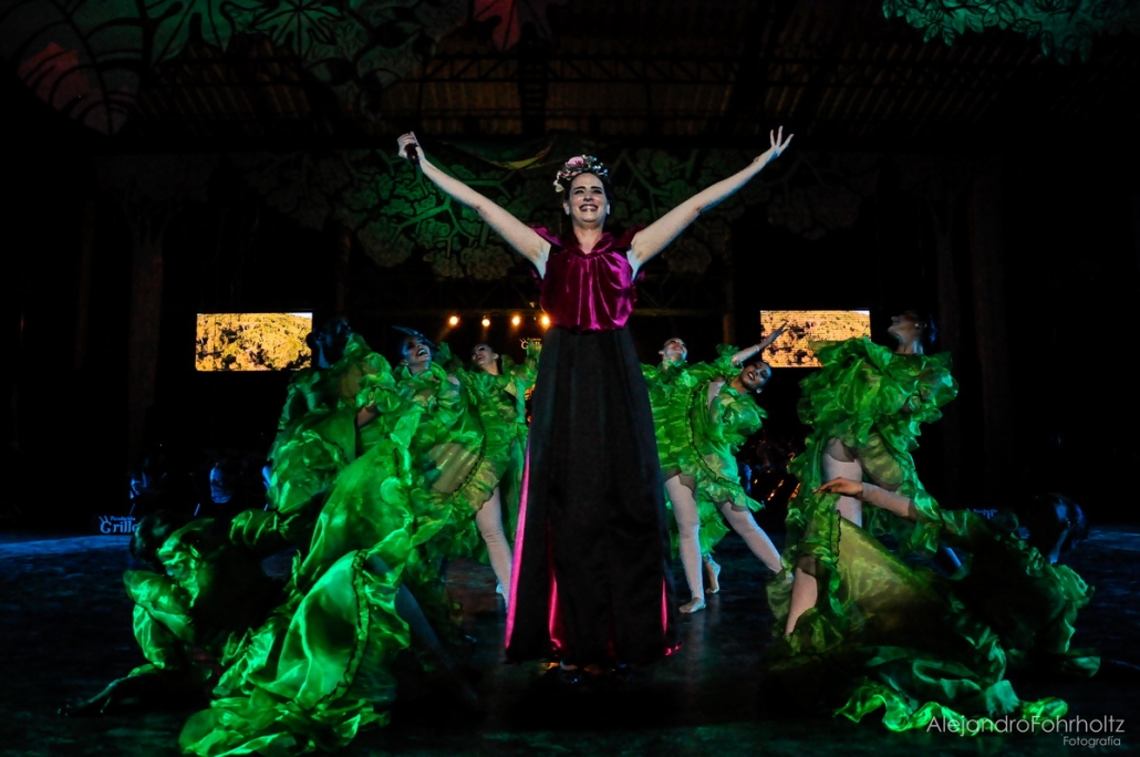 Cantante en escena con los brazos abiertos, iluminada en verde