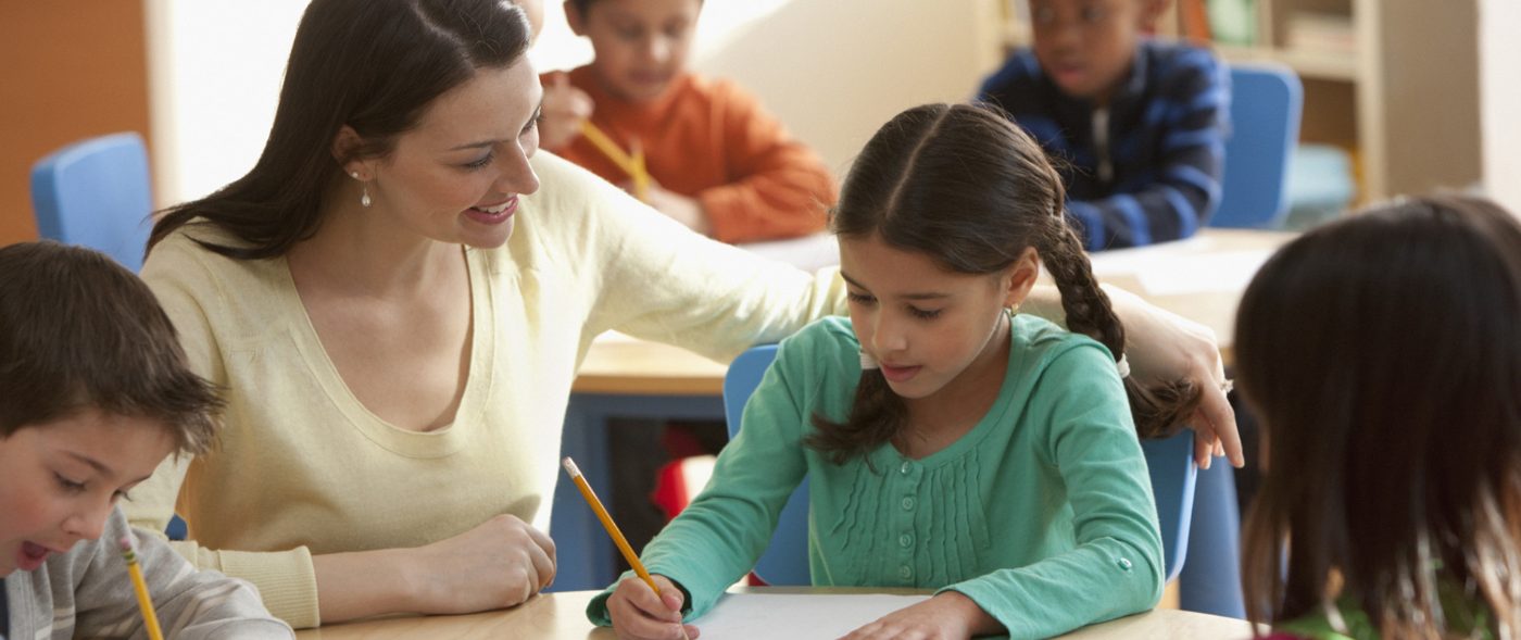 Guía Montessori acompañando a un grupo de niños que escriben en una mesa del aula