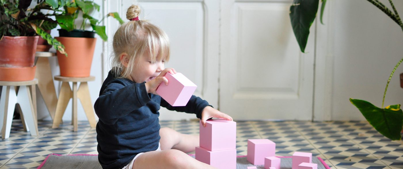 Niña pequeña manipulando los cubos de la torre rosa junto a una estantería